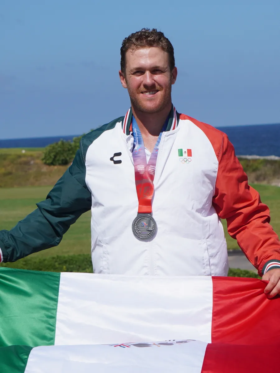 Luis Carrera con la medalla de plata y la bandera de México en un campo de golf
